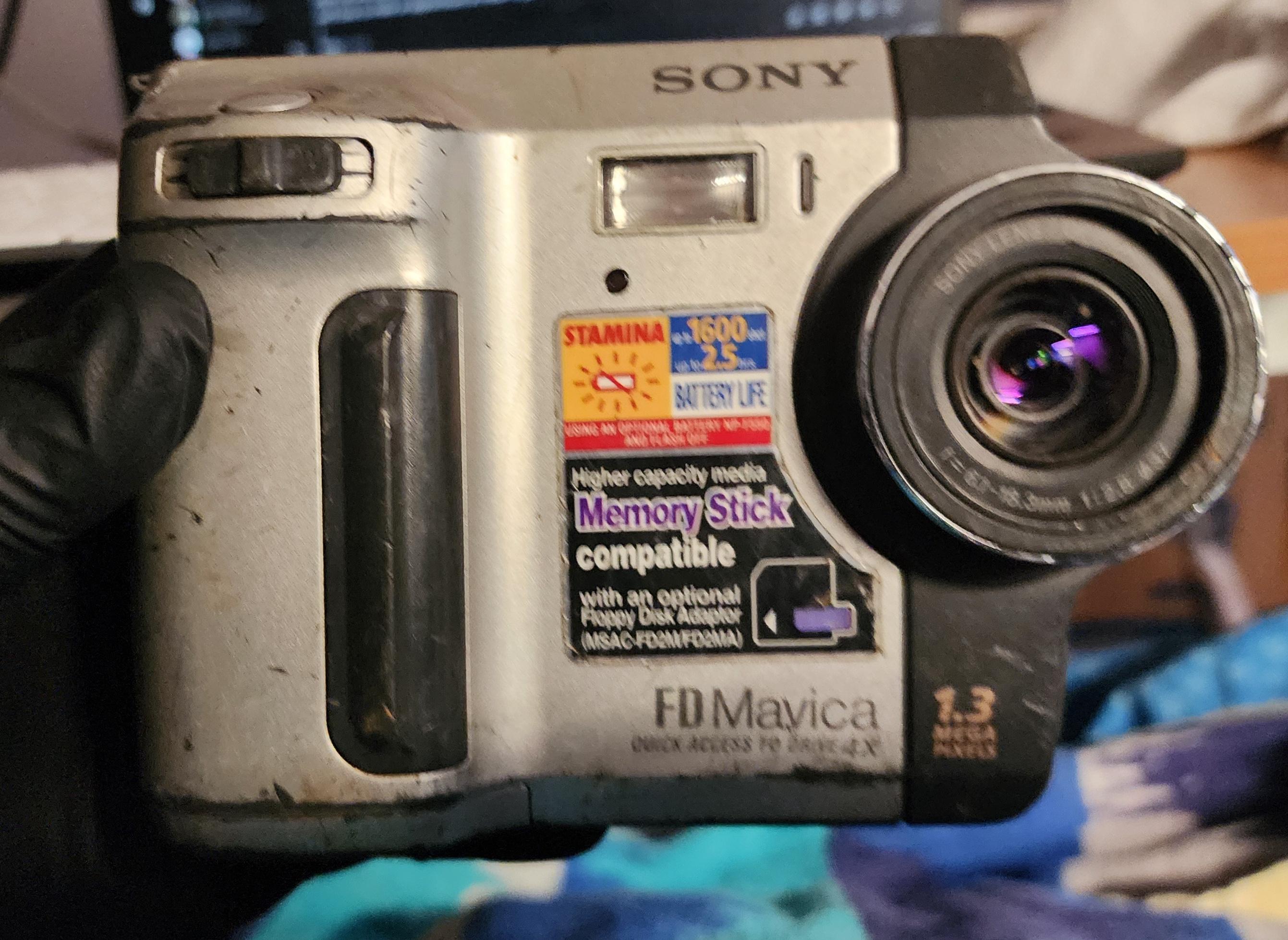 A Sony Mavica MVC-FD87 digital camera, held by a gloved hand. It looks a little beat up and dirty. A Sony Mavica MVC-FD87 digital camera, held by a gloved hand. It looks a little beat up and dirty.
